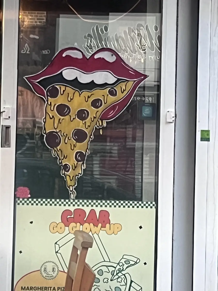 A shop door with a sign showing lips eating a cheesy pizza slice with pepperoni. Below, a poster reads “GRAB GO GLOW-UP” with cartoon pizza images.