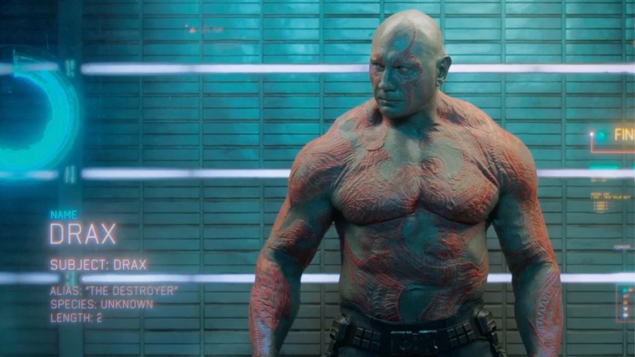 A muscular, shirtless man with red tattoos stands in a futuristic cell. Text on the image reads: “Name: Drax. Subject: Drax. Alias: ‘The Destroyer’. Species: Unknown. Length: ?”. Blue lighting highlights the scene.