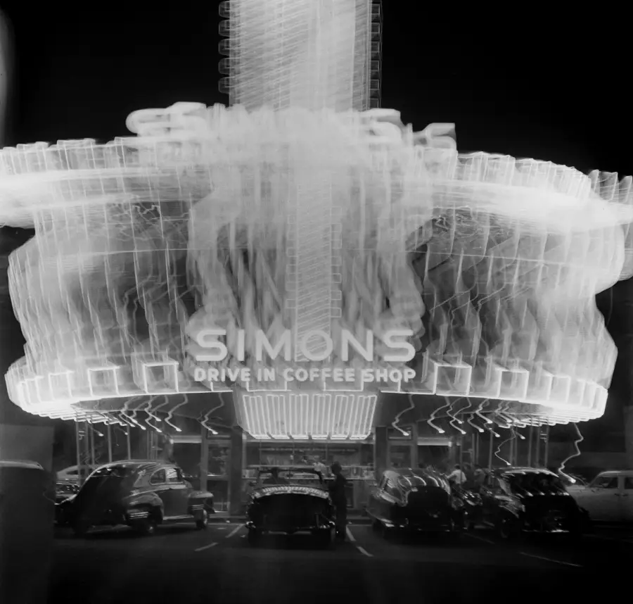 A long-exposure night photo of Simons Drive-In Coffee Shop shows neon lights and cars parked out front, creating a blurred, glowing effect.