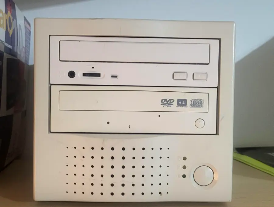 A beige, vintage desktop computer tower with two optical drive bays, a circular power button, and ventilation holes on the front panel, sitting on a wooden surface.
