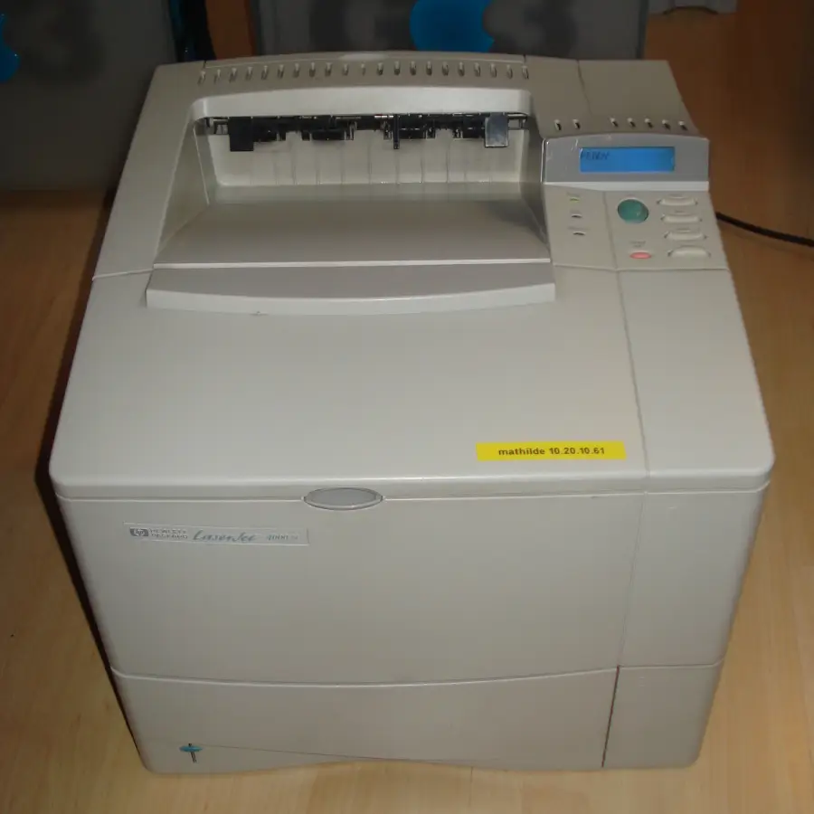 A beige HP LaserJet 4000 series printer sits on a wood floor, displaying buttons and a small screen on the top right, with a yellow label on the front reading “mathilde 10.20.36.61.”