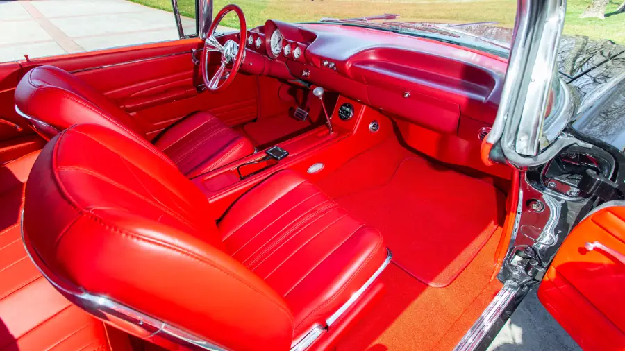 Bright red interior of a classic convertible car, showing leather seats, steering wheel, dashboard, and open driver-side door with sunlight highlighting the details.