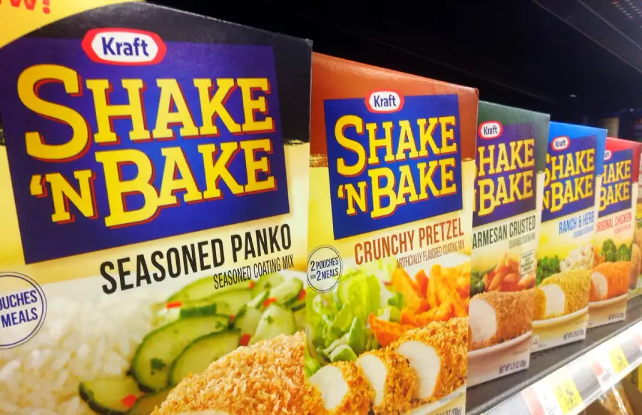 Close-up of Shake ’N Bake products on a grocery shelf, including Seasoned Panko, Crunchy Pretzel, and other varieties in colorful boxes lined up side by side.