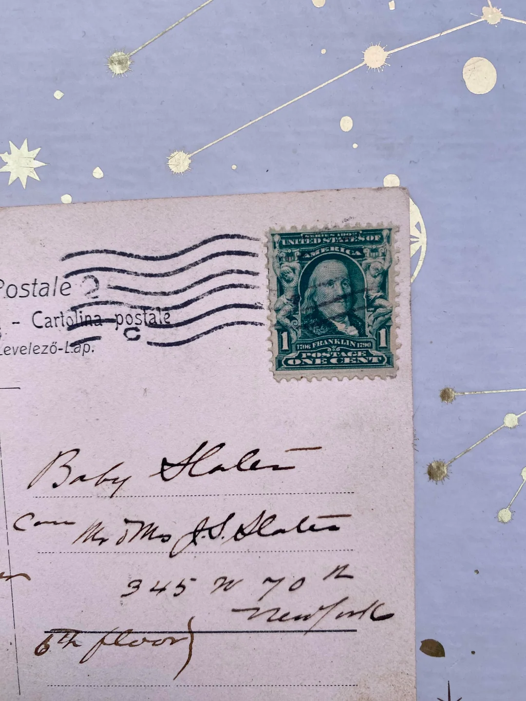 A vintage postcard with a green 1-cent US stamp, handwritten address to “Baby Slater,” and a purple background featuring gold star and constellation designs.
