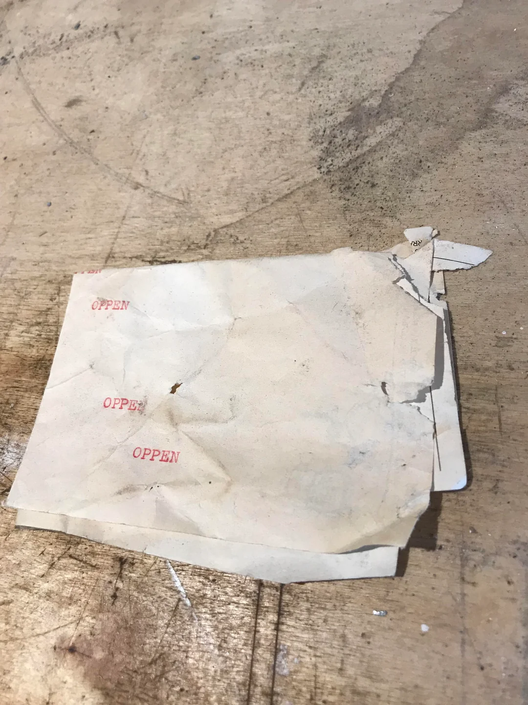 A torn, wrinkled piece of paper with the word “OPPEN” stamped in red three times sits on a scratched, wooden surface.