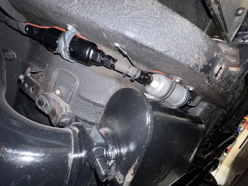 Close-up of a car’s undercarriage showing attached fuel injectors and fuel lines secured with metal brackets and zip ties against the vehicle’s frame.
