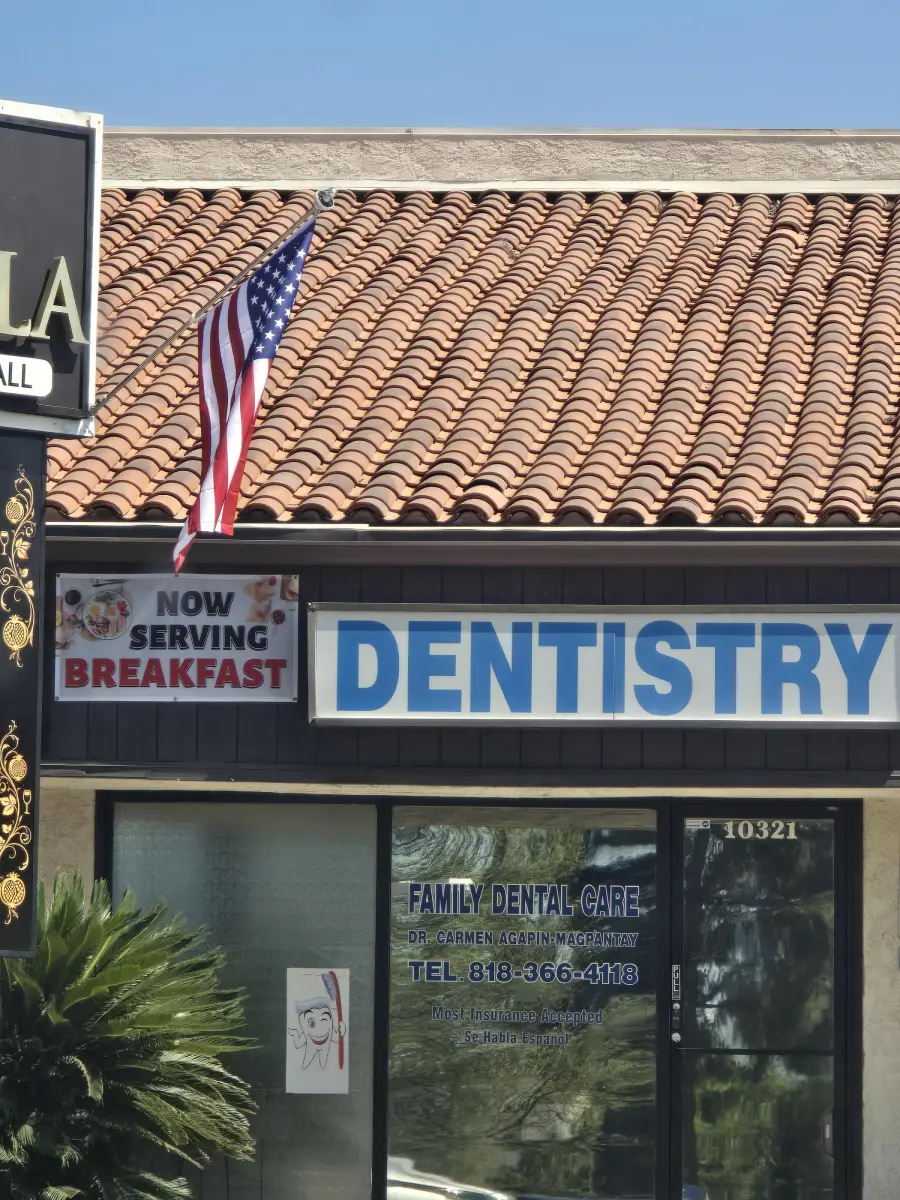 A dentistry office with a sign reading “Now Serving Breakfast” near the entrance, an American flag above, and a “Family Dental Care” sign on the glass door.