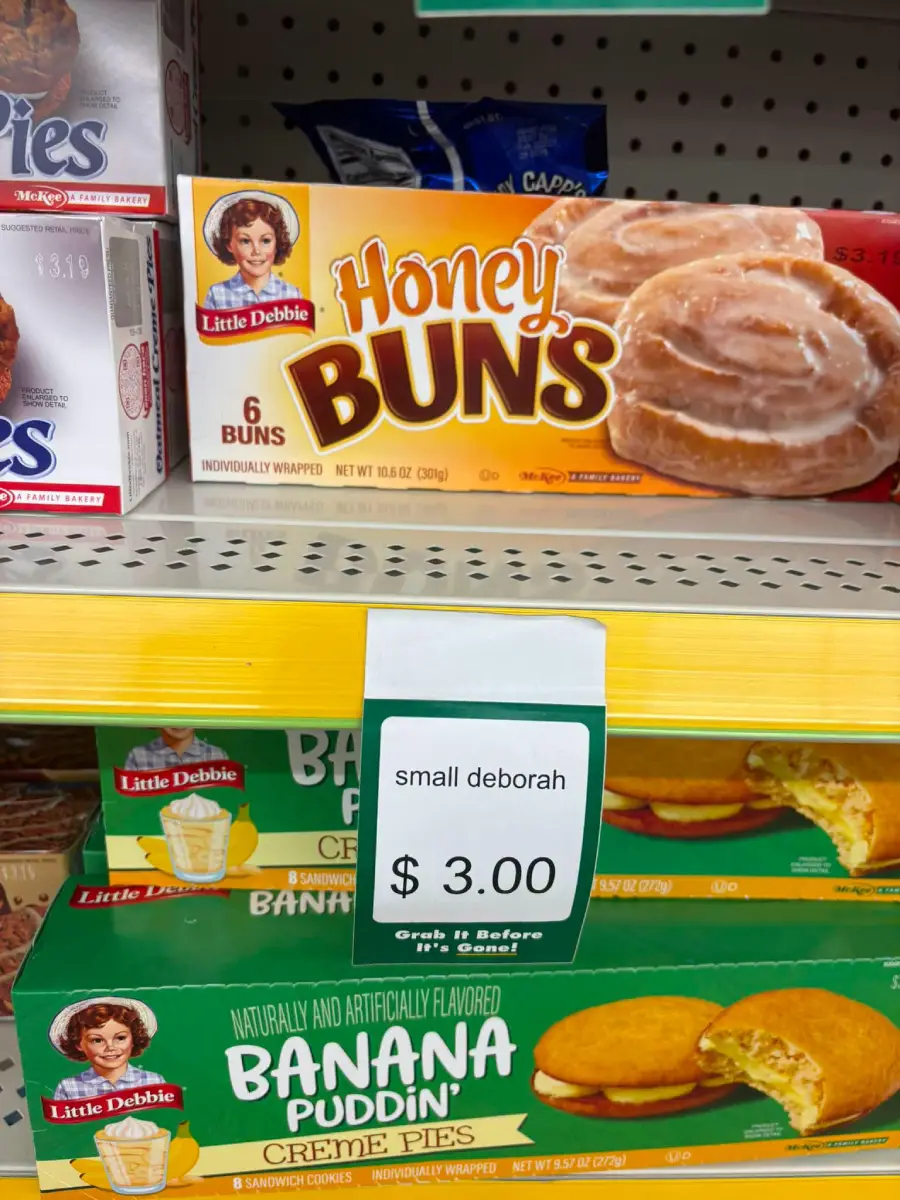 A store shelf displays Little Debbie Honey Buns and Banana Pudding Creme Pies. A sign reads “small deborah $3.00” in front of the Honey Buns.