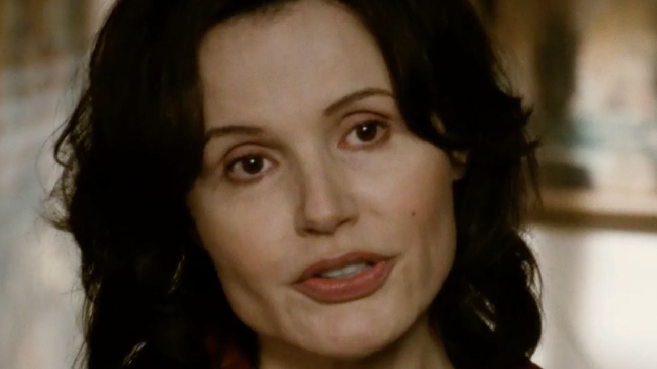 A woman with dark wavy hair and fair skin looks slightly to the side, speaking. The background is blurred, drawing focus to her expressive face.