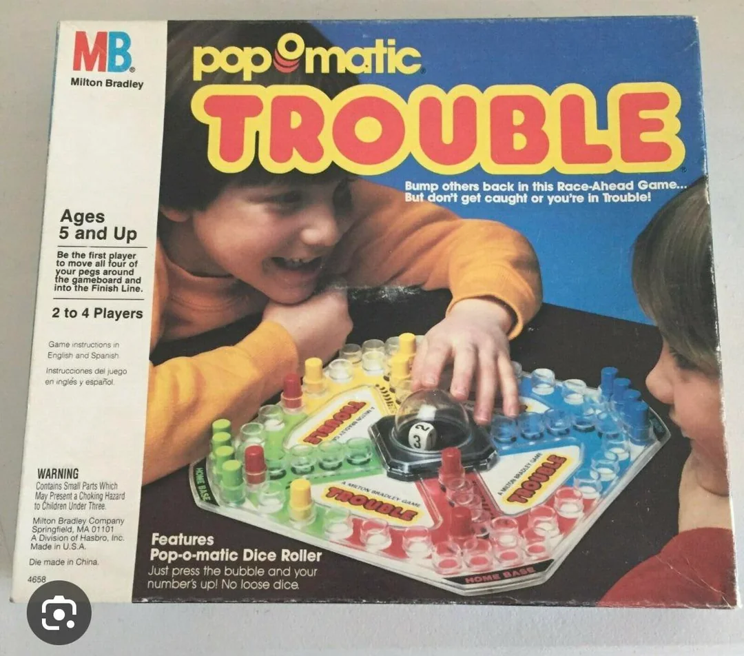 A box of Milton Bradley’s Pop-O-Matic Trouble game shows two kids playing with the colorful board and dice bubble. The box features the game’s name, instructions, and player age range.