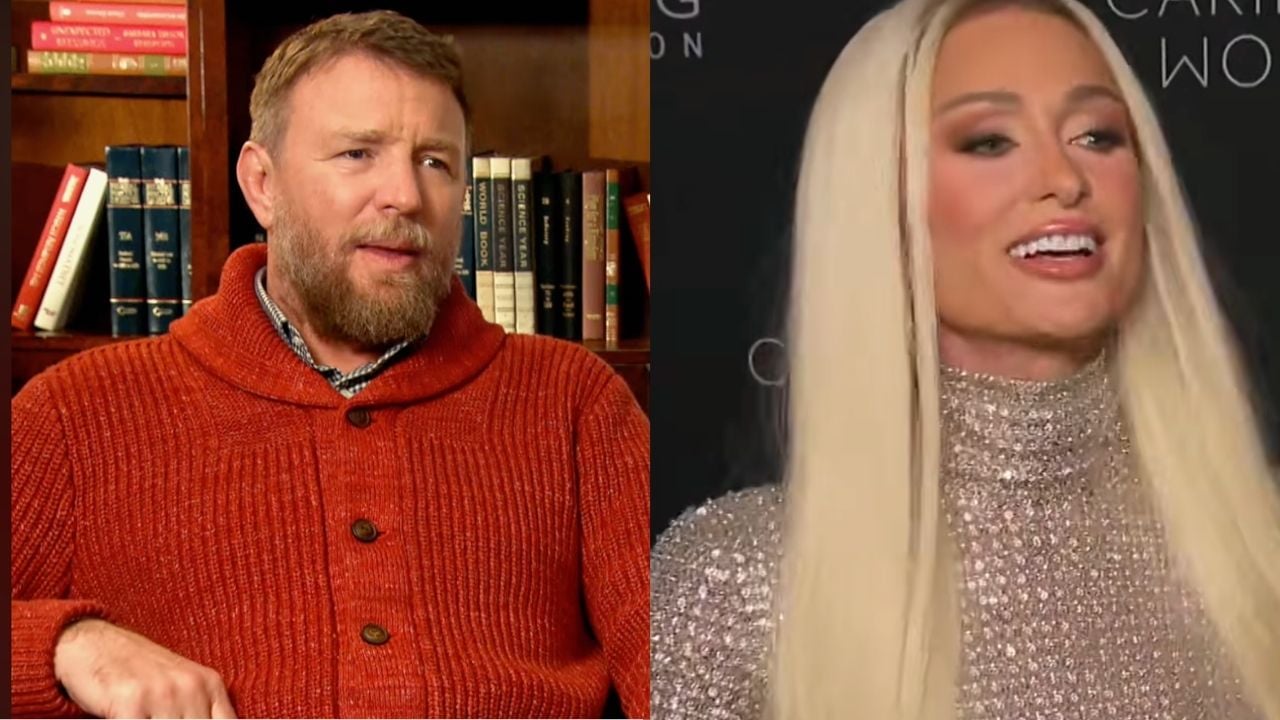 A man with a beard wearing a red sweater sits by a bookshelf; beside him, a woman with long blond hair and a sparkling silver dress smiles against a dark background.