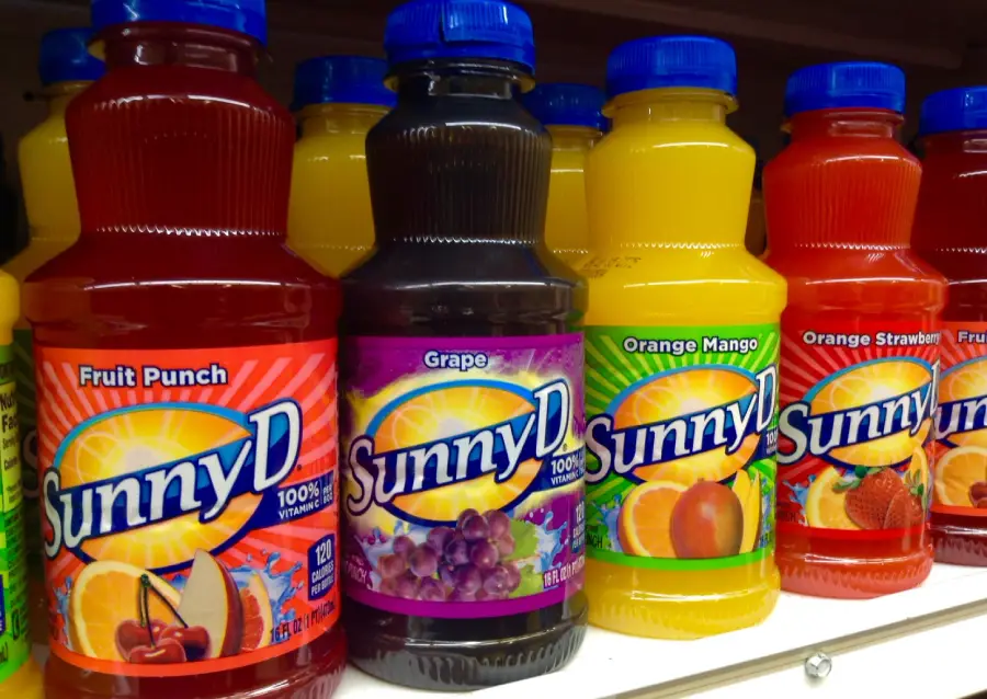 Bottles of SunnyD juice in various flavors, including Fruit Punch, Grape, Orange Mango, and Orange Strawberry, are displayed on a store shelf.