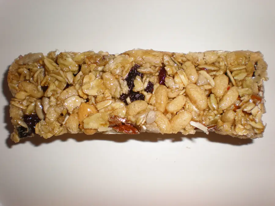 A close-up of a granola bar with oats, nuts, seeds, and dried fruit on a plain white background.