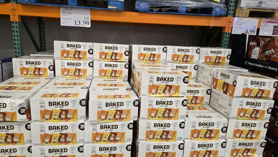 Stacks of large boxes of Frito-Lay Baked chips variety packs on a store shelf. Price tags are visible above the boxes, showing a price of $13.99.