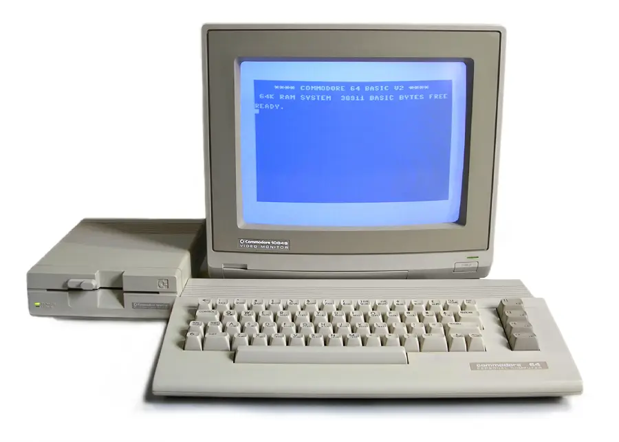 A vintage Commodore 64 computer setup with a monitor displaying blue text, a keyboard, and a floppy disk drive, all in beige.