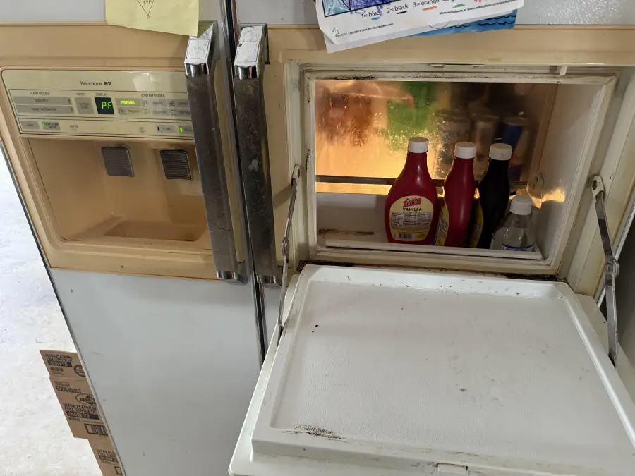 Refrigerator with a hatch open on the freezer door, revealing bottles of condiments and a few other items inside, with the door tray flipped down as a shelf.