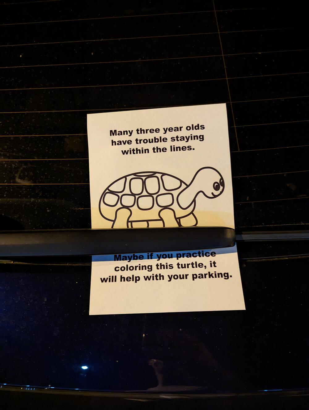A paper with a turtle drawing is placed under a car wiper. It reads, “Many three year olds have trouble staying within the lines. Maybe if you practice coloring this turtle, it will help with your parking.”