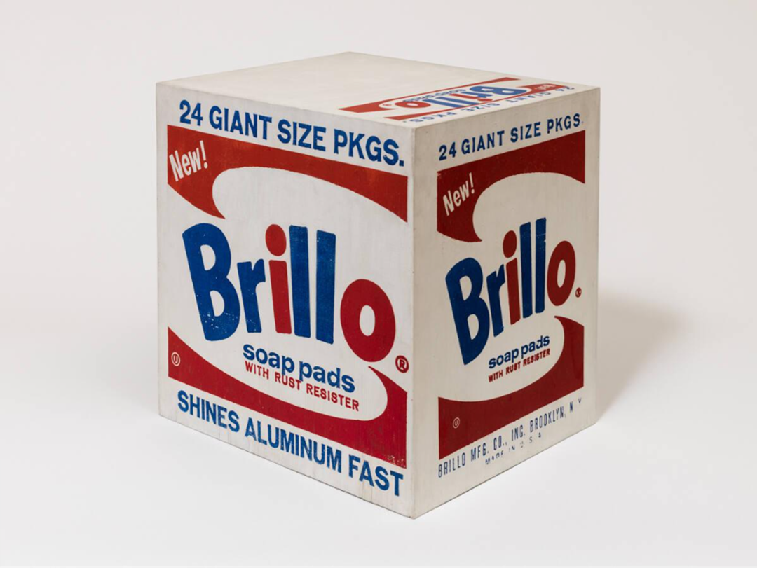 A large, cube-shaped box labeled “Brillo soap pads,” featuring bold red and blue text, advertising “24 giant size pkgs.” and “shines aluminum fast” on a white background.