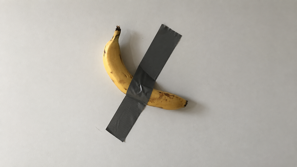 A single yellow banana is taped to a plain white wall with a diagonal strip of grey duct tape, resembling the artwork “Comedian” by Maurizio Cattelan.