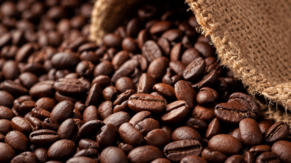 Close-up of roasted coffee beans spilling out from a burlap sack, showing their shiny, dark brown surfaces and textured details.