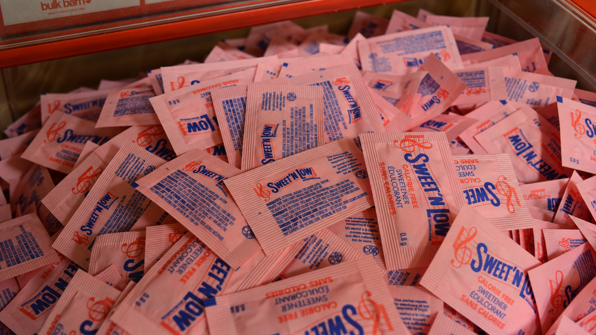 A large pile of pink Sweet’N Low zero calorie sweetener packets fills a container.