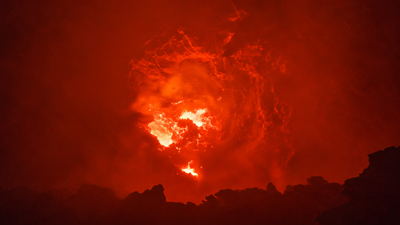 Fiery lava glows intensely, surrounded by dark, jagged rocks and thick red-orange smoke, creating a dramatic volcanic eruption scene.