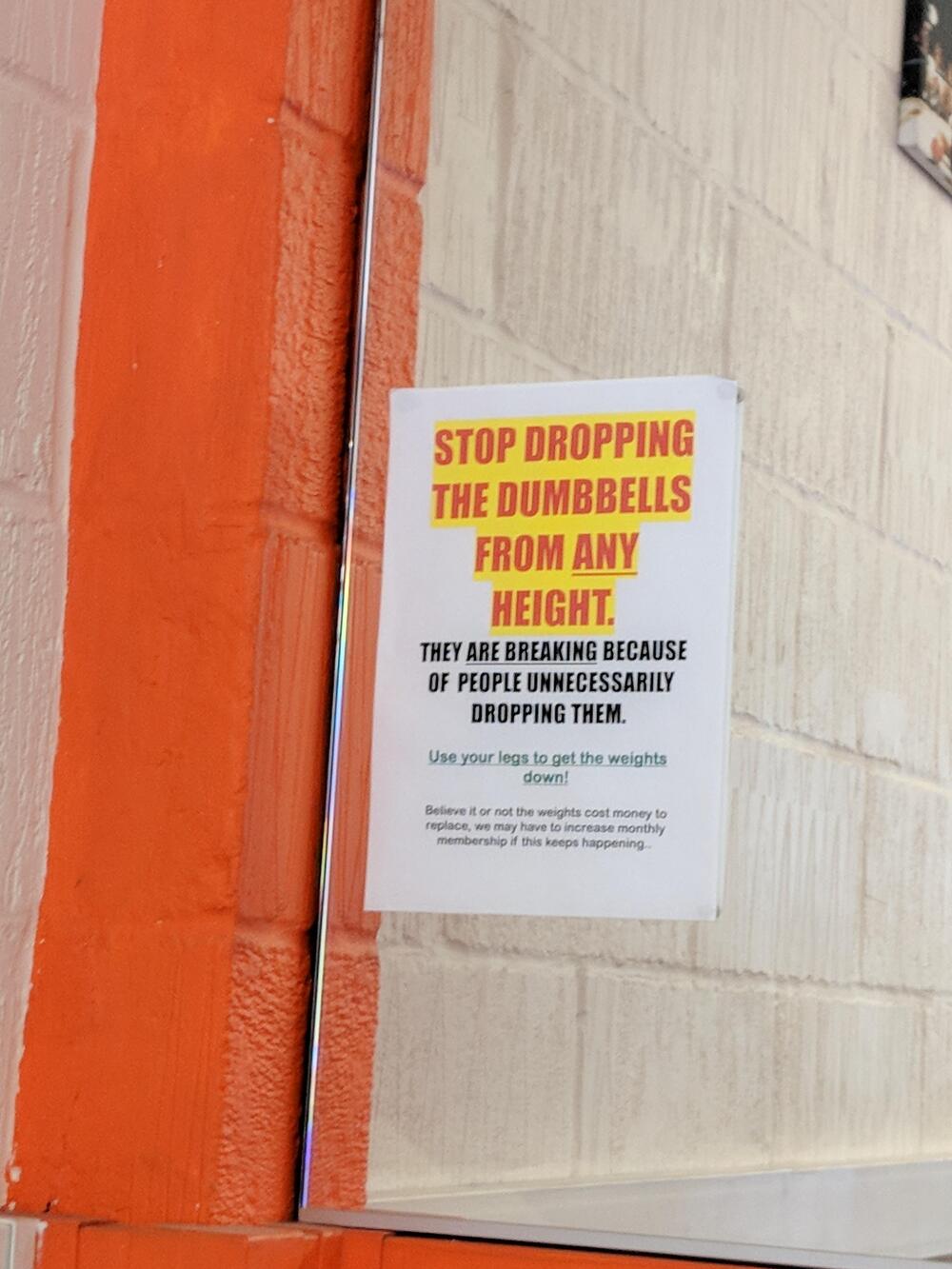 A sign on a gym wall reads: “Stop dropping the dumbbells from any height. They are breaking because of people unnecessarily dropping them. Use your legs to set the weights down!”