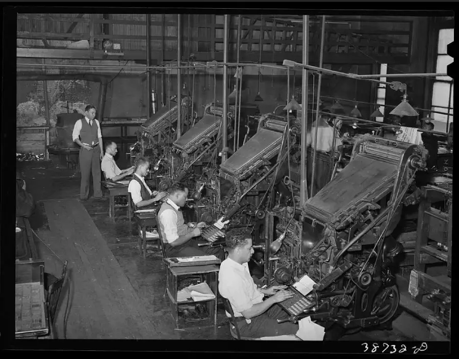 Several men operate large typesetting machines in a factory-like room with high ceilings and exposed beams. One man stands, supervising, while the others sit and work at their stations.