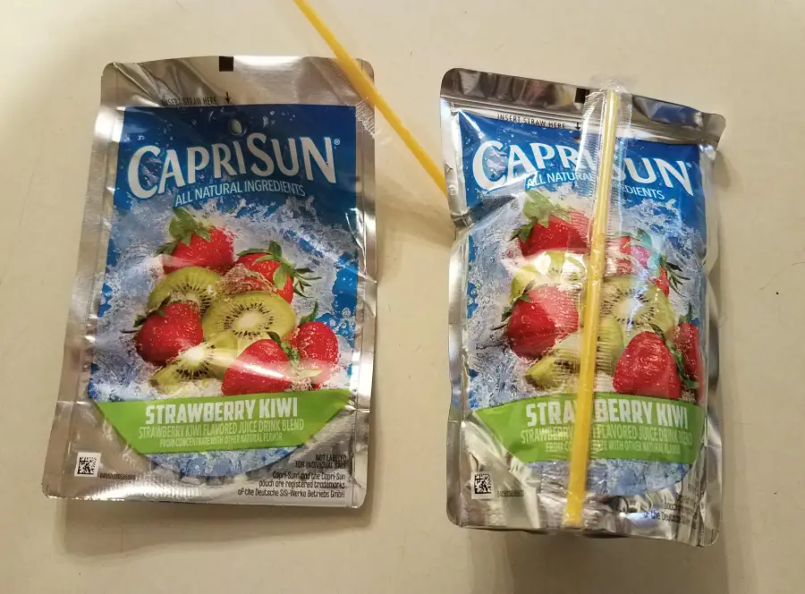Two Capri Sun Strawberry Kiwi drink pouches sit side by side. The pouch on the right has a straw inserted incorrectly through the side, while the left pouch is unopened with the straw still attached.