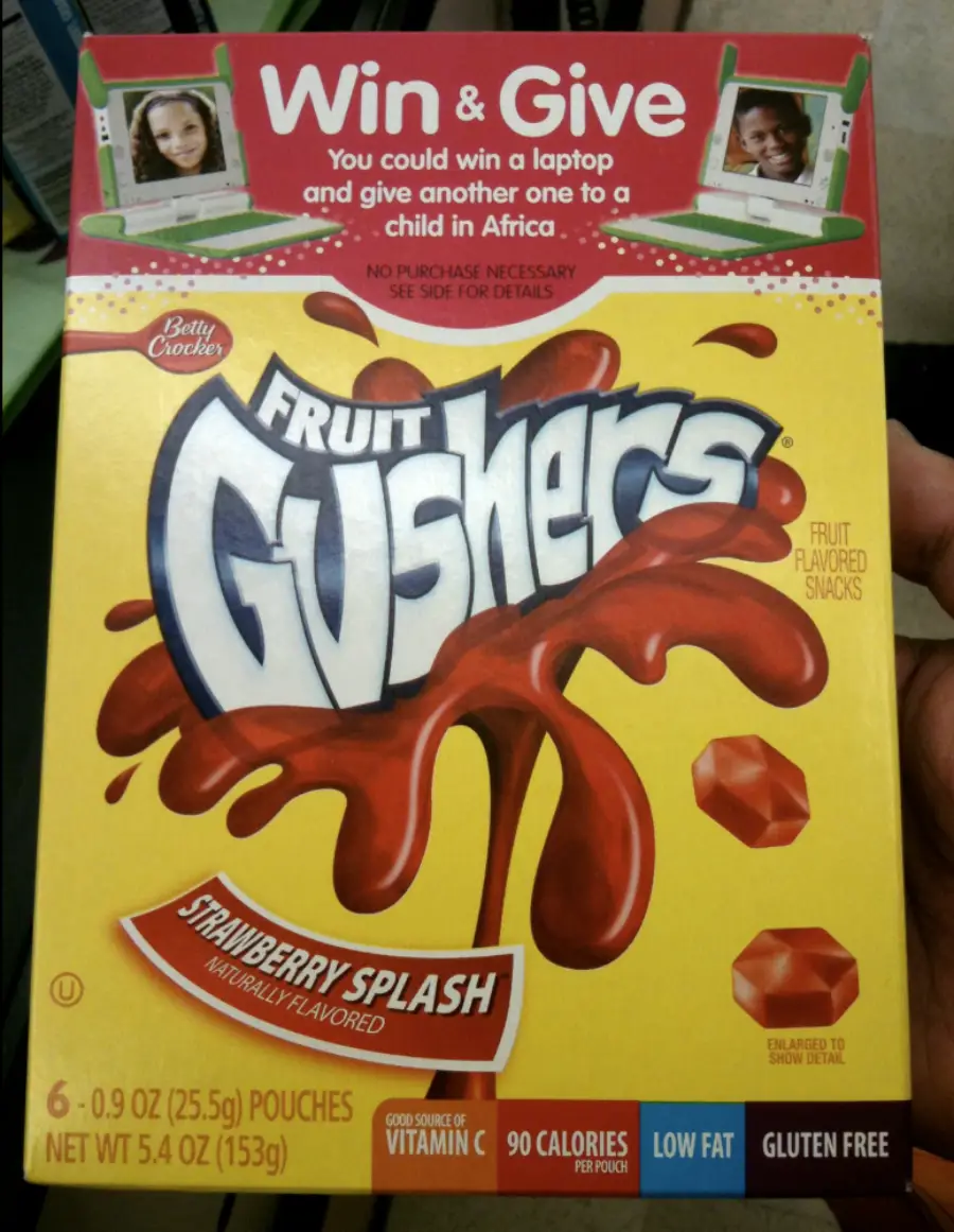 A box of Betty Crocker Fruit Gushers, Strawberry Splash flavor, featuring a “Win & Give” laptop giveaway promotion. The bright box has images of red gusher candies and splashes.