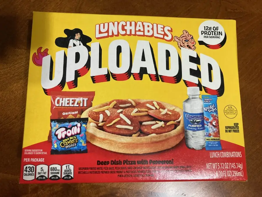 A Lunchables Uploaded box featuring deep dish pizza with pepperoni, Cheez-It crackers, Trolli mini candy, bottled water, and Kool-Aid drink mix on a wooden table.