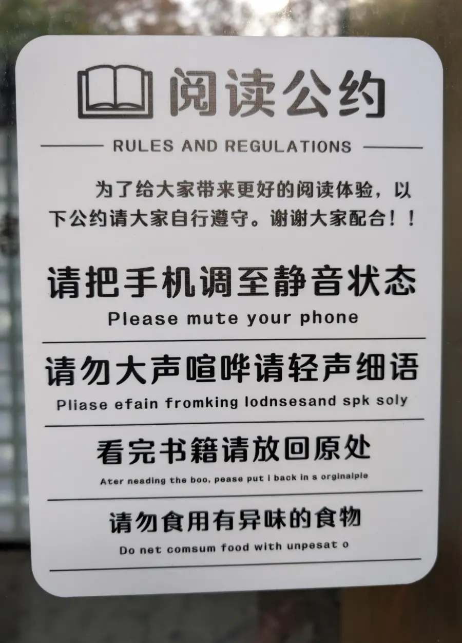 A sign with Chinese and English text displaying reading room rules, including muting phones, speaking softly, returning books, and not consuming food with unpleasant odors.