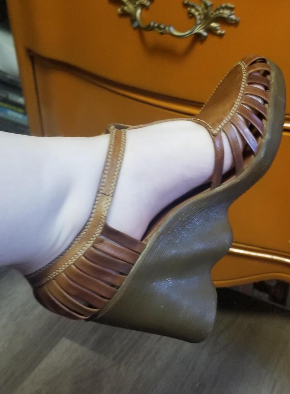 A close-up of a foot wearing a brown strappy wedge sandal with a thick, sculpted sole, in front of an orange drawer.