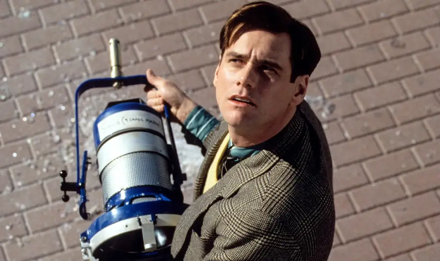 A man in a suit looks up while holding a large stage light on a pedestrian brick path, appearing surprised or concerned.