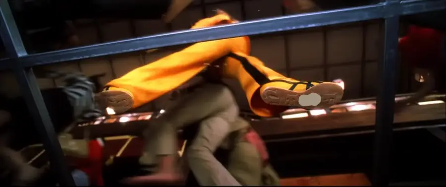 Low-angle shot through a glass floor showing a person in yellow pants and black shoes walking above, with other figures visible beneath the glass.