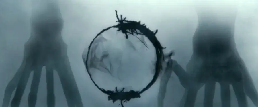 A smoky, abstract circle floats in the center, flanked by two large, shadowy, hand-like figures on each side, set against a misty, gray background.