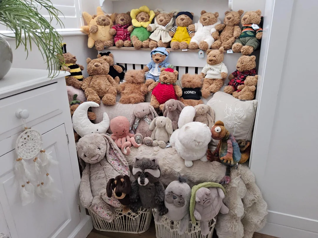 A collection of teddy bears and various stuffed animals arranged on shelves and baskets in a cozy nook beside a white cabinet and dreamcatcher.