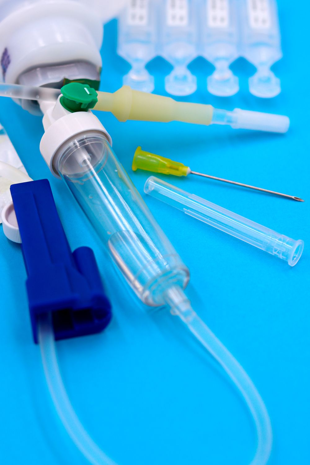 Close-up of medical supplies including a needle, syringe, tubing, and connectors on a blue background.