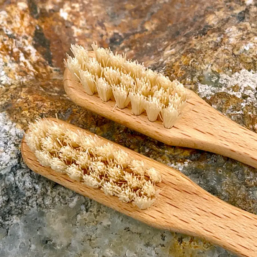 Two wooden toothbrushes with light-colored bristles resting on a textured stone surface. The bristles appear natural and slightly uneven, emphasizing the eco-friendly design of the toothbrushes.