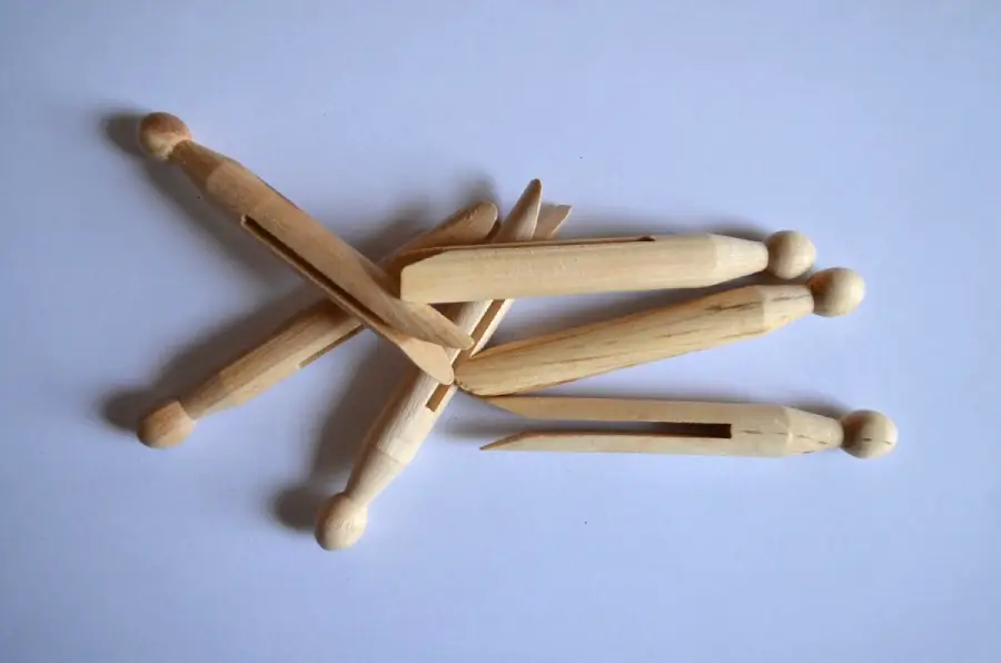 Four wooden clothespins are scattered on a white surface, arranged in a loose pile with some overlapping each other.