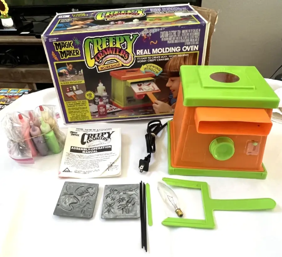 Creepy Crawlers Magic Maker set with oven, molds, instructions, colored goop bottles, a tool, lightbulb, and box featuring a child making toy bugs. Everything is arranged neatly on a table.