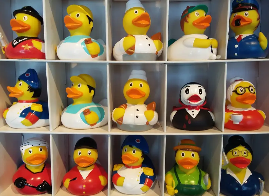 A display case with shelves holding rubber ducks dressed as various professionals and characters, including a chef, doctor, police officer, and others, each wearing unique costumes and accessories.