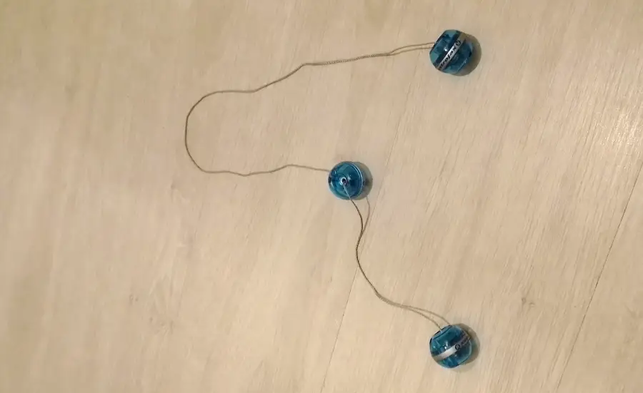 Three blue plastic yo-yos connected by a string are arranged on a light wooden floor, forming a loose triangular shape.