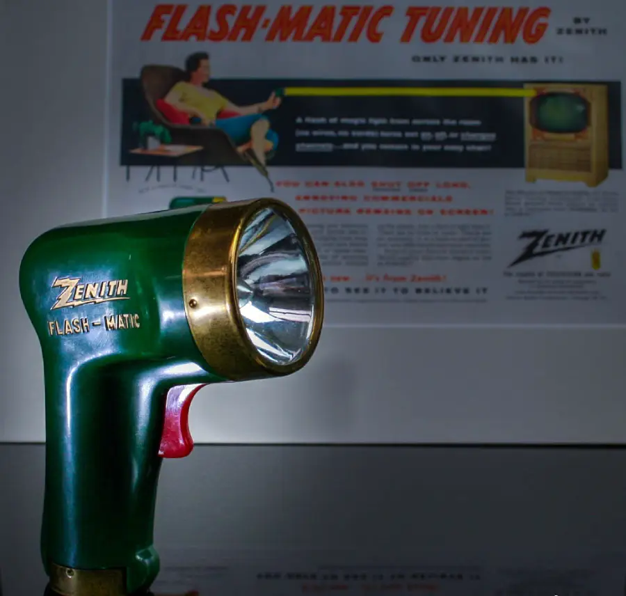 A vintage Zenith Flash-Matic remote control is displayed in the foreground, with an old advertisement for Flash-Matic Tuning featuring a TV and a person in the background.