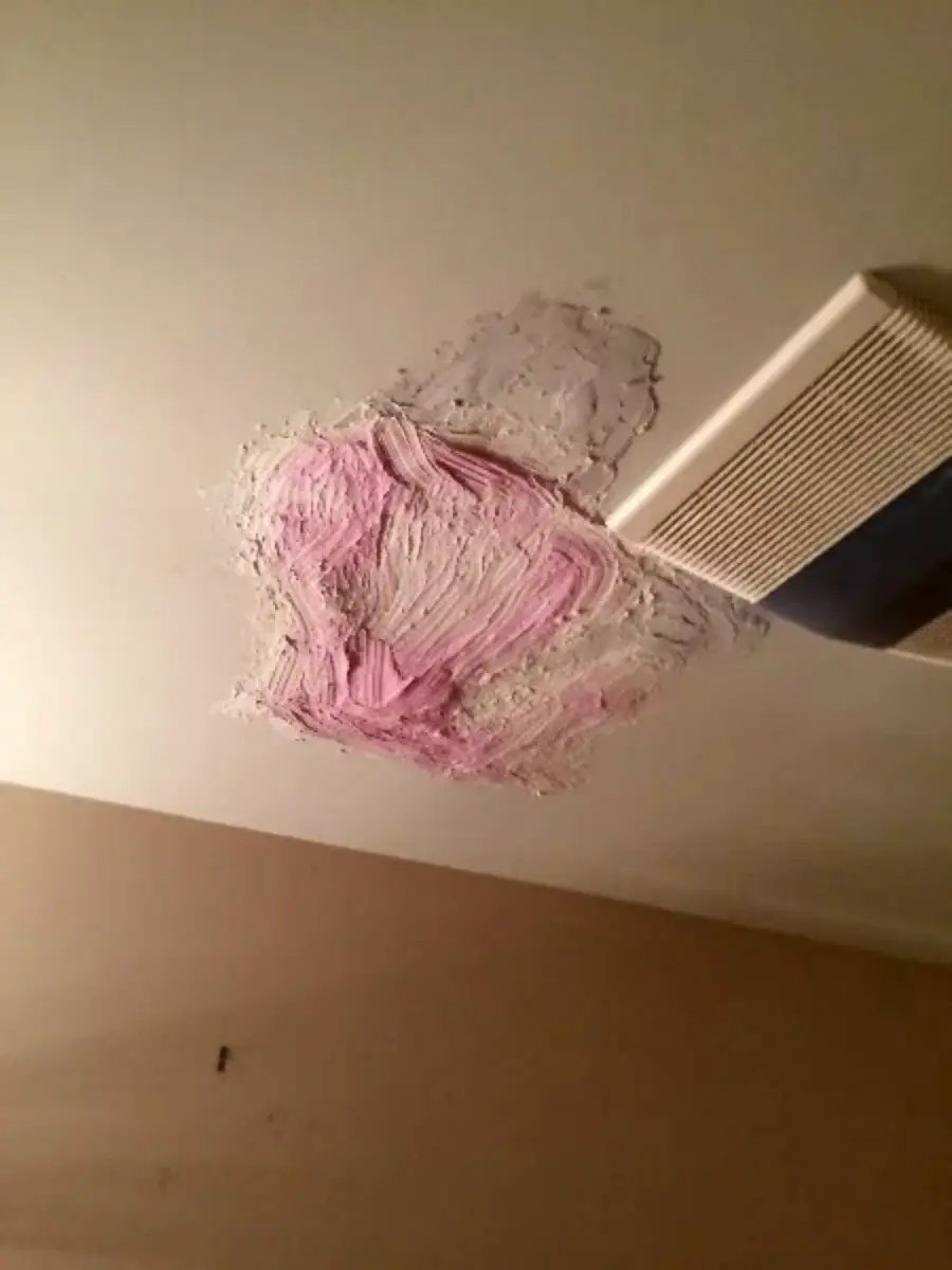 A ceiling with a rough patch of pink spackle around a repaired area next to a white air vent. The patch appears uneven and unfinished.