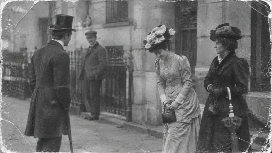 Two women in vintage dresses and hats greet a man in a suit and top hat on a city sidewalk; a man stands by a fence in the background. The image appears old and worn.