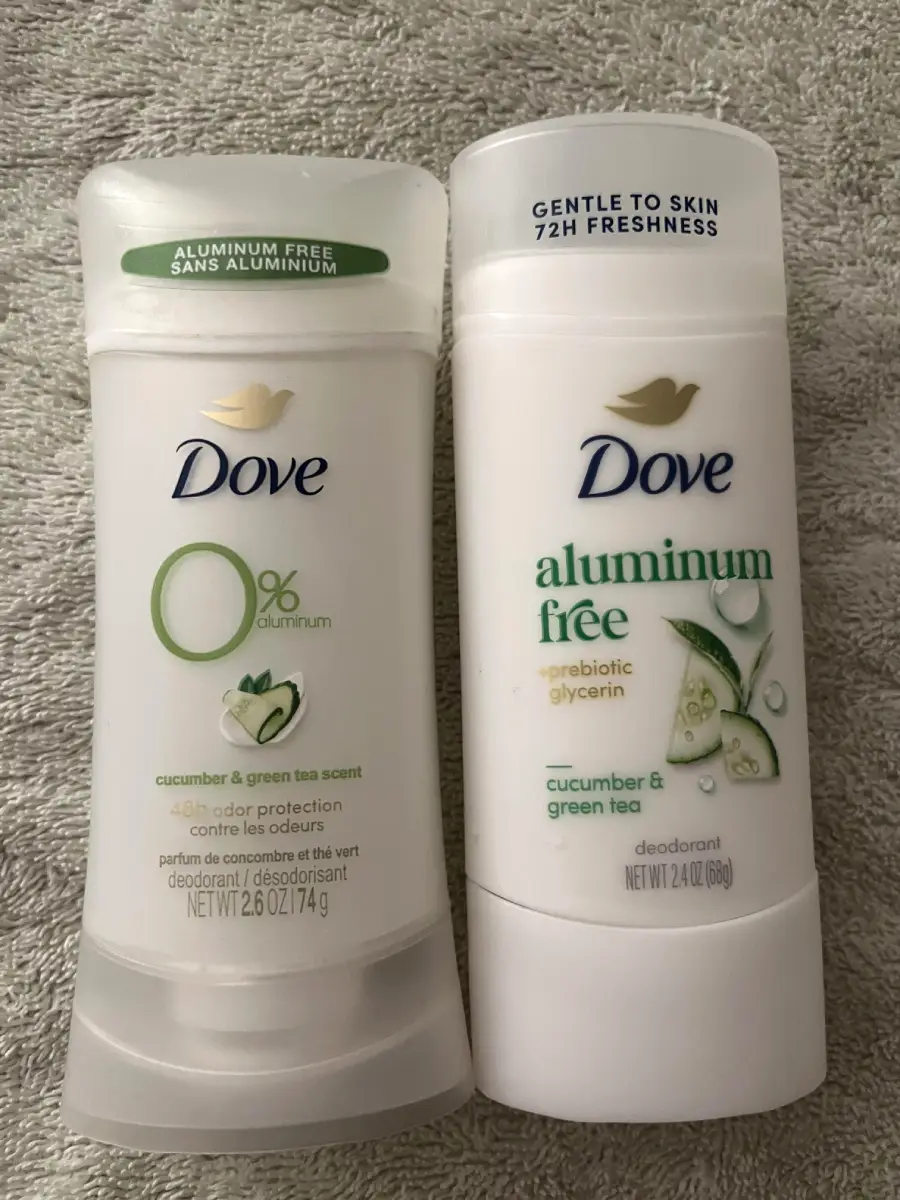 Two Dove deodorant sticks on a towel, both labeled aluminum free. The left stick says “0% aluminum” and features cucumber and green tea. The right stick also mentions cucumber and green tea, and highlights “gentle to skin.”