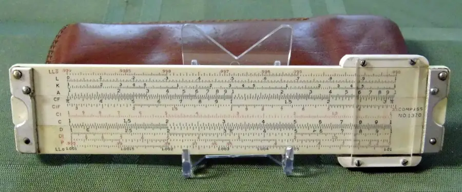 A vintage slide rule with a leather case is displayed on a green surface, supported by a clear plastic stand.