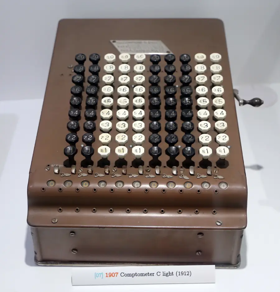 A vintage Comptometer adding machine from 1912, with eight columns of round black and white number keys and a side lever, on display in a museum.