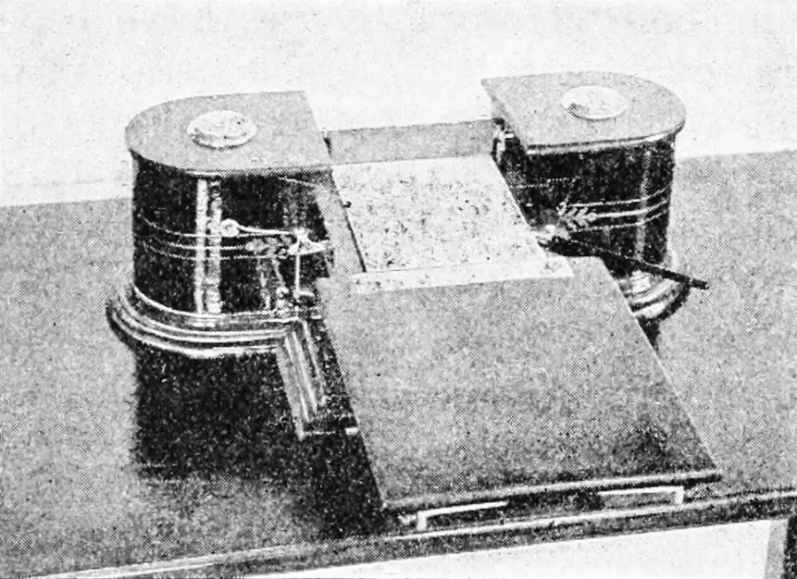 Black and white photo of an early automatic writing machine with two round sections and a flat writing surface, featuring gears and a lever mechanism.